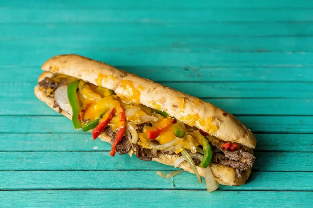 Cheesesteak on a hoagie roll with melted cheese and peppers, on a teal wooden board