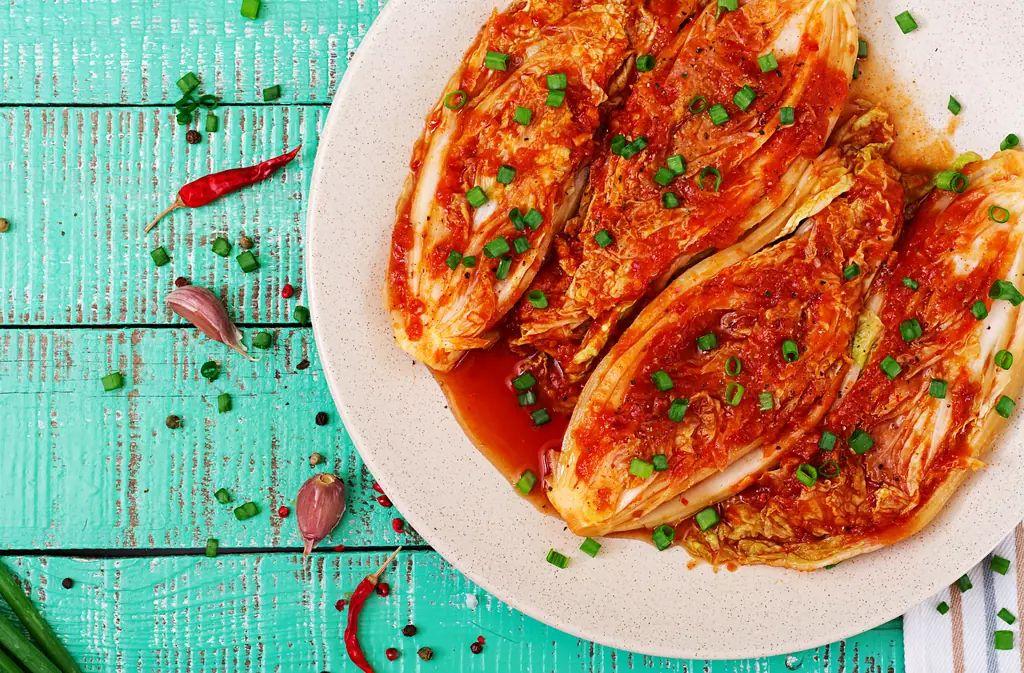 Napa cabbage kimchi on a white plate, on a turquoise wooden table with chili peppers and garlic