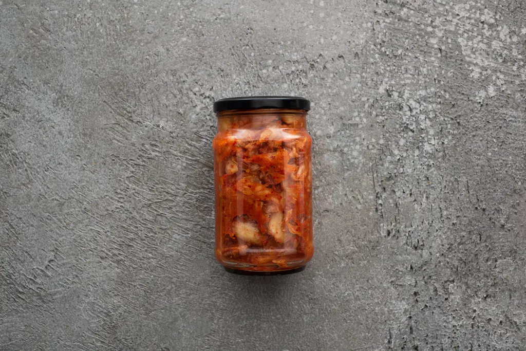 A jar of red kimchi on a grey stone surface